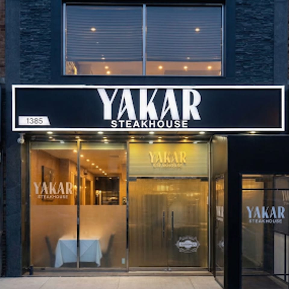 Front entrance of YAKAR Steakhouse with illuminated signage and glass doors.